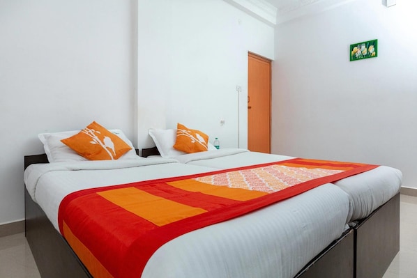 A neatly made bed with white bedding and orange pillows, a red and orange blanket, and a green artwork on the wall.