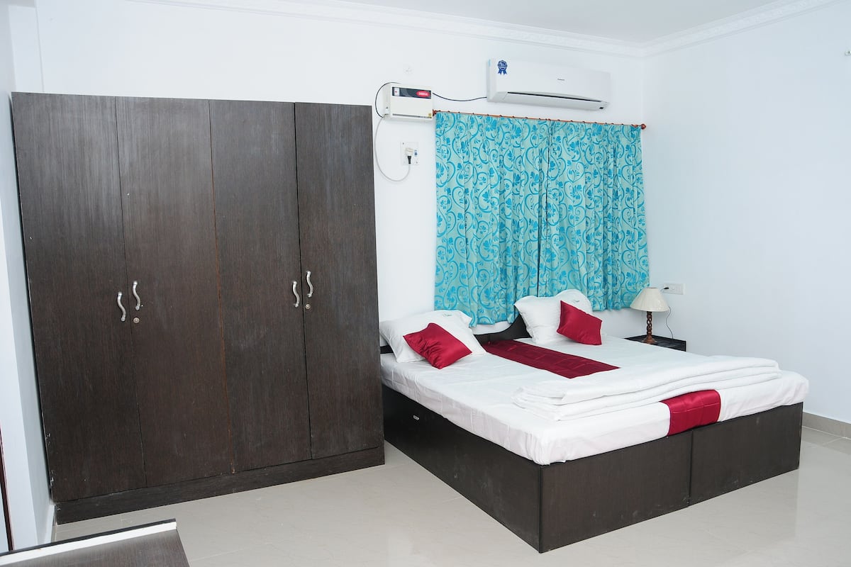 A bedroom with a bed, a wardrobe, an air conditioning unit, and a curtain.