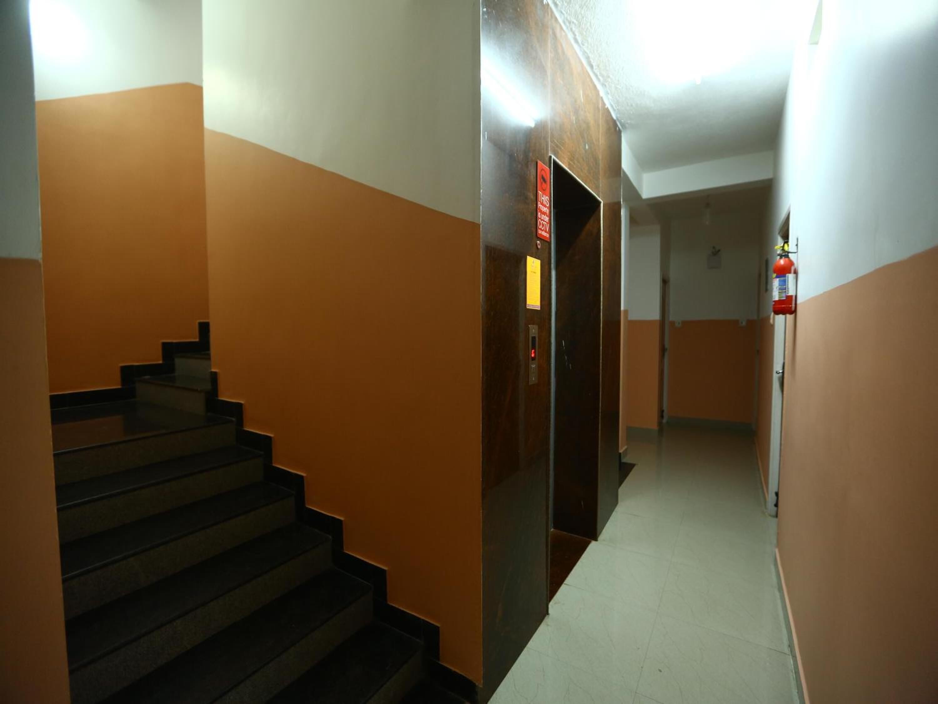 A hallway with a staircase, a fire extinguisher, and a door with a security camera sign.