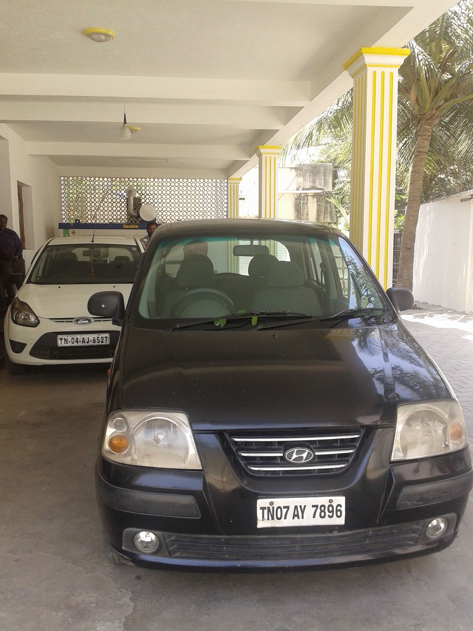 A black car with a visible license plate in a covered parking area with yellow pillars.