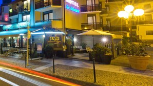 A hotel with a neon sign, a restaurant, and outdoor seating. - Logis Hôtel le Littoral (Evian-les-Bains)