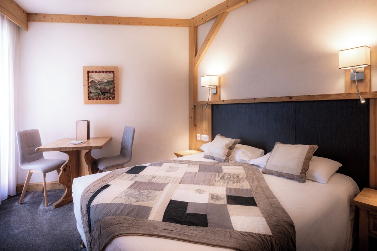 Habitación de hotel con una cama grande, un escritorio, dos sillas y dos lámparas fijadas a la pared.