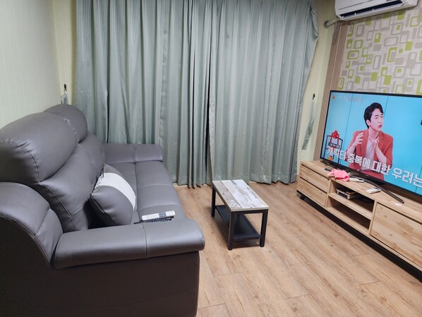 A living room with a grey sofa, a wooden coffee table, and a TV on a wooden stand.