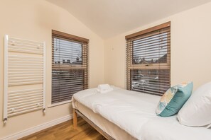 A bedroom with a bed, two windows with blinds, a radiator, and a wooden floor. - Glandore Lodge (Belfast)