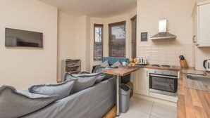 A compact kitchen with a built-in oven, a dining table, and a grey sofa. - Glandore Lodge (Belfast)