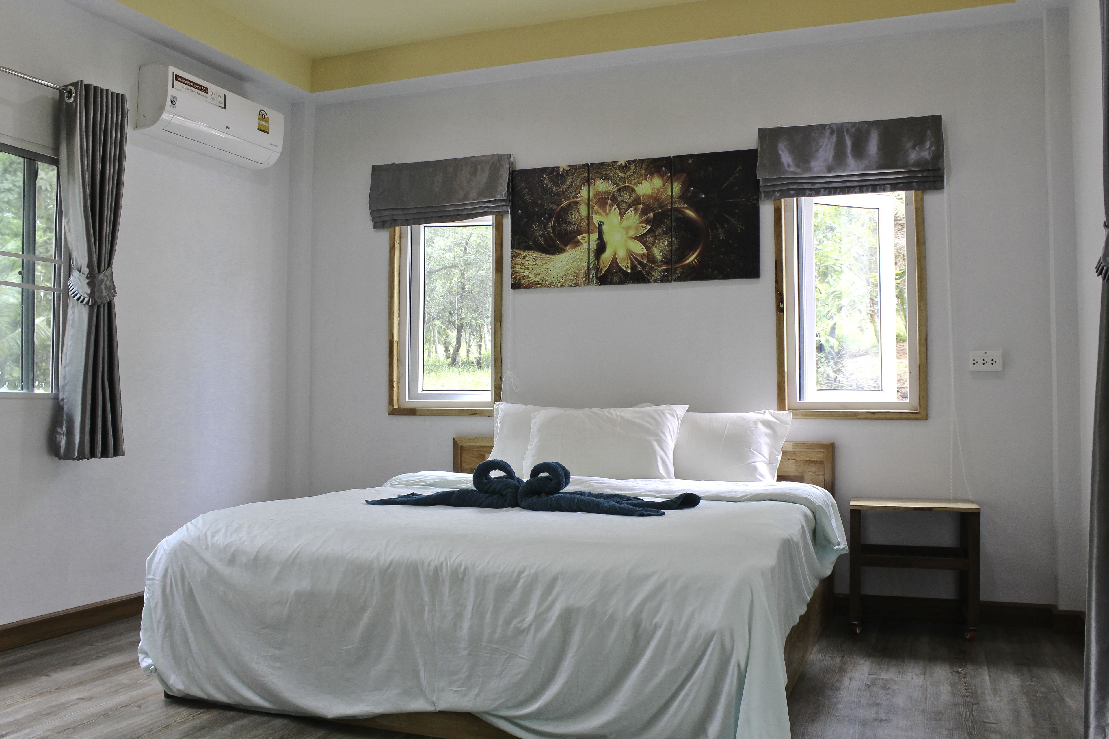 Habitación de hotel con cama, dos ventanas, aire acondicionado y un cuadro en la pared.