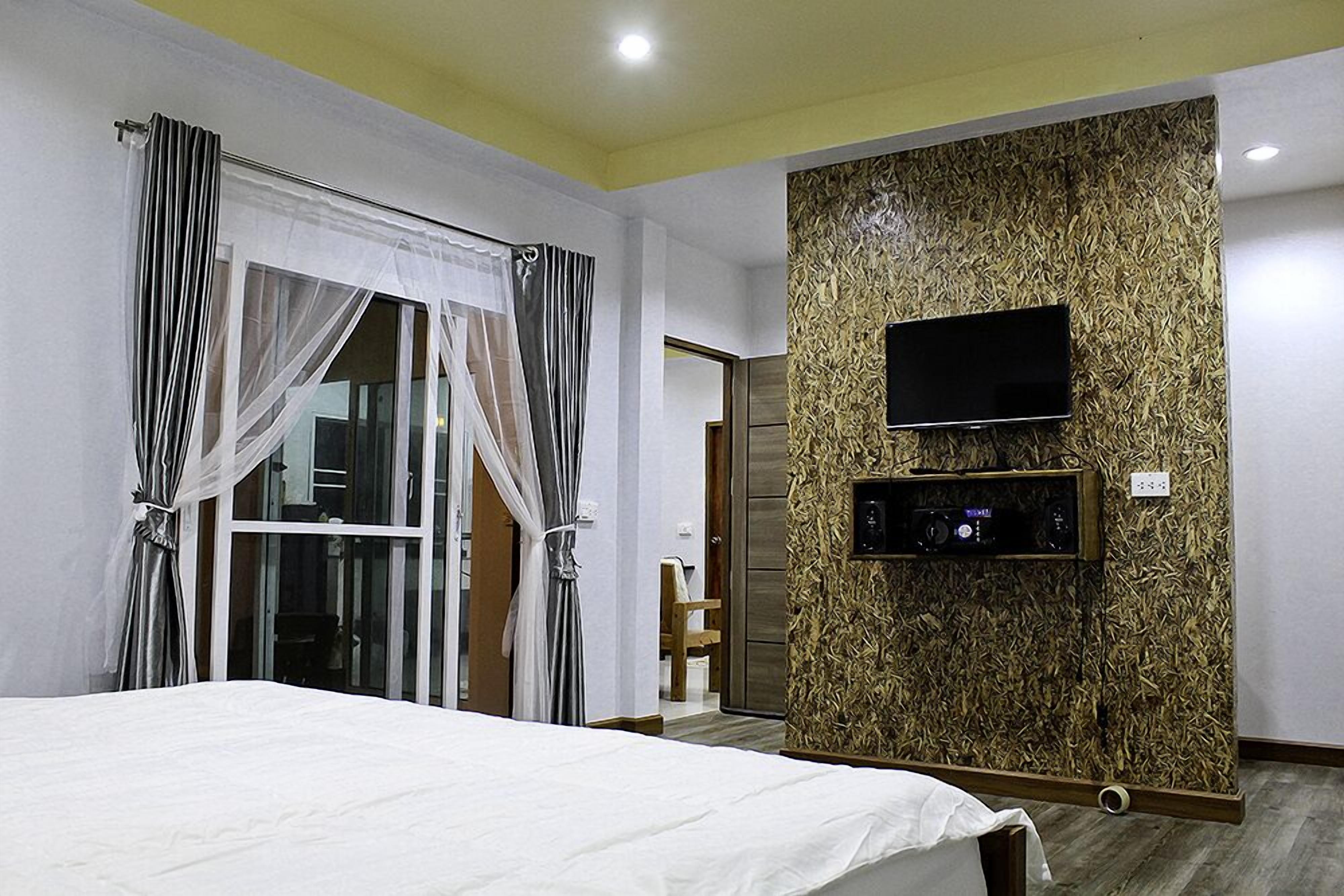 A bedroom with a bed, a TV mounted on a textured wall, and a sliding door with curtains.