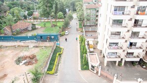 Un edificio residencial de varios pisos con balcones, una calle en frente y vegetación circundante.