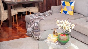 Una sala de estar con un sofá, una mesa de centro de vidrio, una mesa de comedor con sillas y un mapa mundial en la pared.