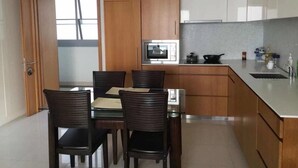 A modern kitchen with wooden cabinets, a built-in microwave, a stove, and a dining area with a table and chairs. - NorthPoint Pattaya with Sea View (Pattaya)