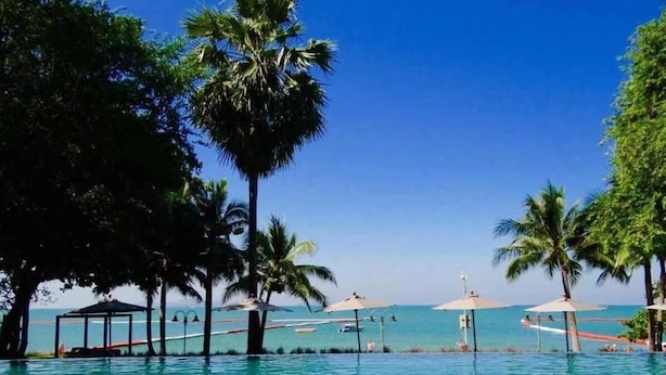 A clear blue pool surrounded by palm trees and beach umbrellas. - NorthPoint Pattaya with Sea View (Pattaya)