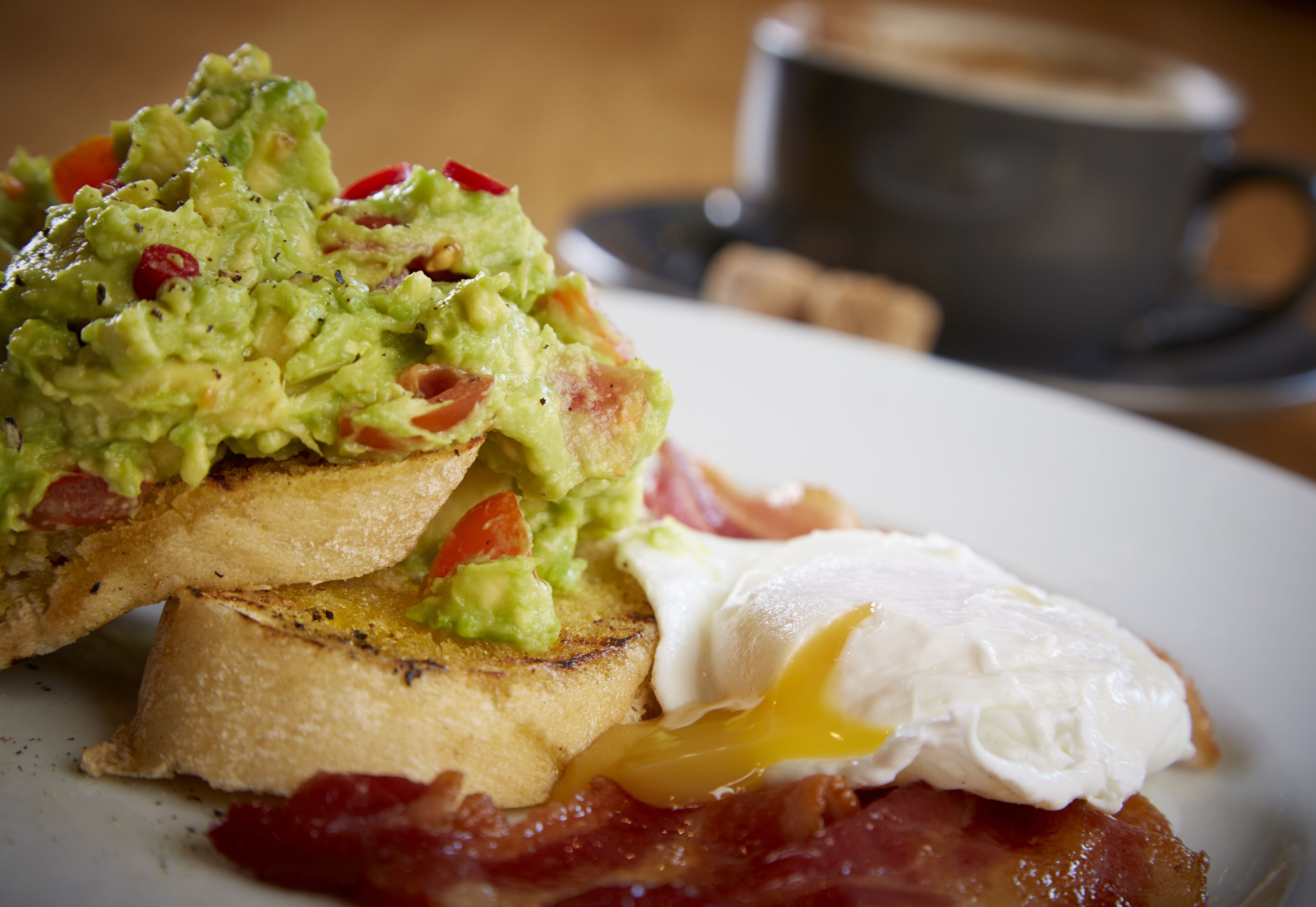 A breakfast plate with toast, avocado, bacon, and a poached egg.