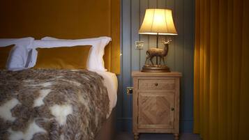 A bed with a patterned blanket, a nightstand with a lamp and a deer statue, and a fur rug on the floor.
