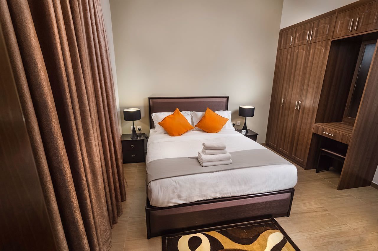 A neatly made bed with two pillows, a bedside table with a lamp, and a wardrobe.