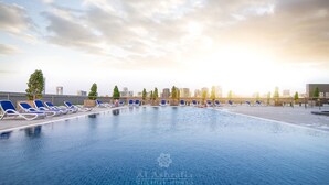 Piscina no terraço com cadeiras de descanso azuis e um horizonte urbano ao fundo.