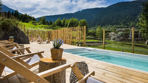 A wooden deck with lounge chairs and a swimming pool, surrounded by a wooden fence and a mountainous landscape. - Mountain Hostel Tarter (El Tarter)