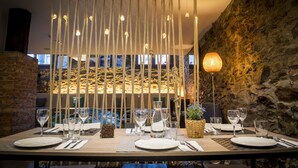 A dining table set with plates, glasses, and cutlery, with a rope curtain overhead and a stone wall in the background. - Mountain Hostel Tarter (El Tarter)