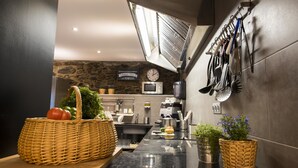 A modern kitchen with a stone wall, a microwave, and a clock. There are baskets of vegetables and a sink. - Mountain Hostel Tarter (El Tarter)