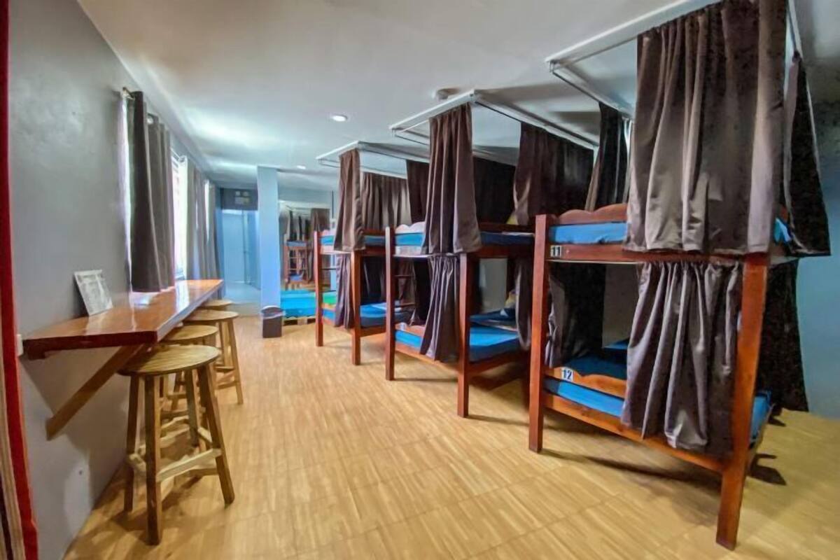 A room with bunk beds, a wooden desk, and stools.