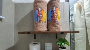 A bathroom with a wooden shelf holding two towels labeled 'West Coast Beach House'. Below the shelf, there is a toilet paper roll, a small potted plant, and a note. - West Coast Beach House (Moalboal)
