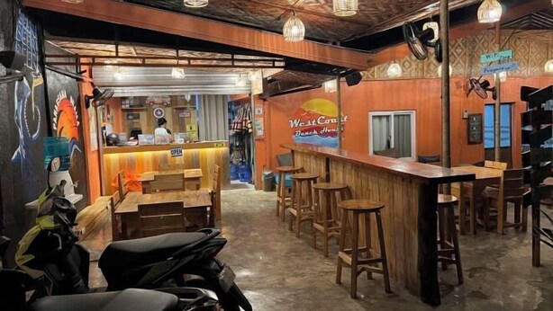 A restaurant interior with a bar area, wooden furniture, and a counter with a sign reading "West Coast Beach House." - West Coast Beach House (Moalboal)