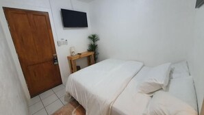 A bedroom with a bed, a wooden door, a small table with a plant, and a TV mounted on the wall. - West Coast Beach House (Moalboal)