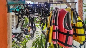 A rack of life jackets and helmets for rent, with a sign indicating the rental price. - West Coast Beach House (Moalboal)