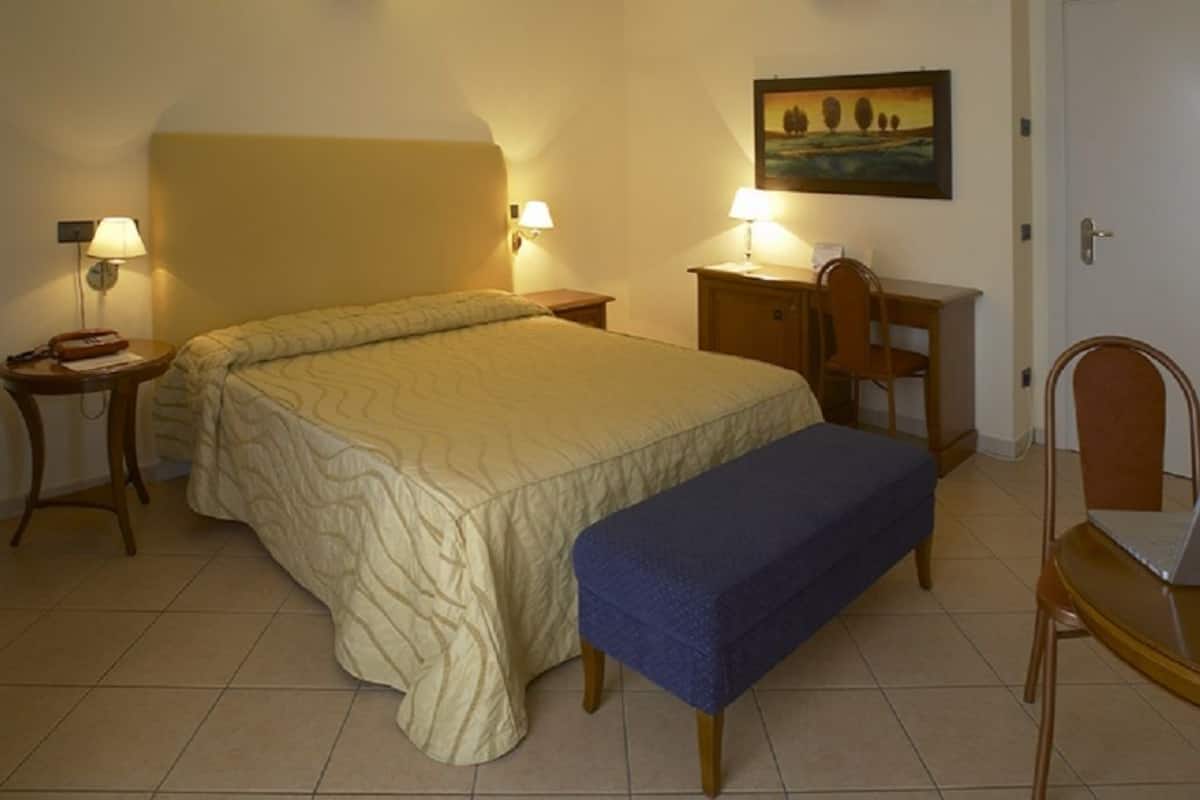 A hotel room with a large bed, a desk, a chair, and a bench.