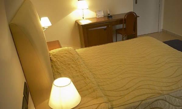 Habitación de hotel con cama, dos lámparas de noche, un escritorio con silla y una mesita con lámpara.
