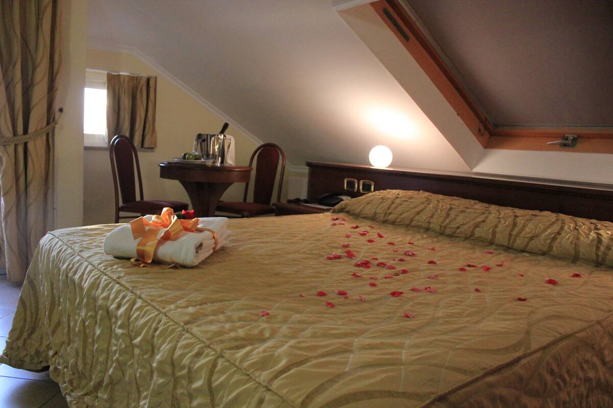A hotel room with a large bed, a desk, a chair, and a nightstand.