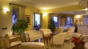 Un vestíbulo de hotel con una zona de estar, ventanas amplias y plantas en macetas.