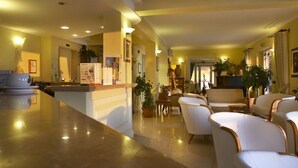 Un vestíbulo de hotel con un mostrador de recepción de mármol, sofás de cuero blanco y plantas en macetas.