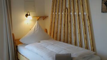 A single bed with white bedding, a wooden headboard, a wall-mounted light, and a wooden slat partition.