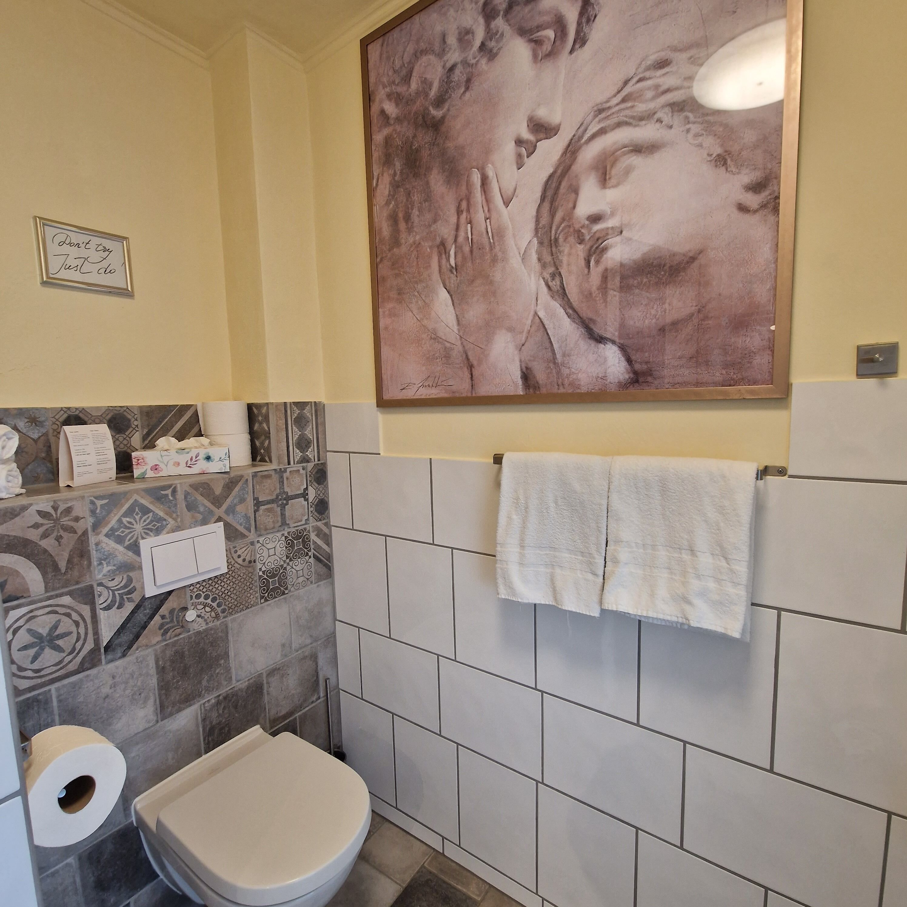 Un baño con inodoro, baldosas estampadas, toallero y una obra de arte enmarcada en la pared.