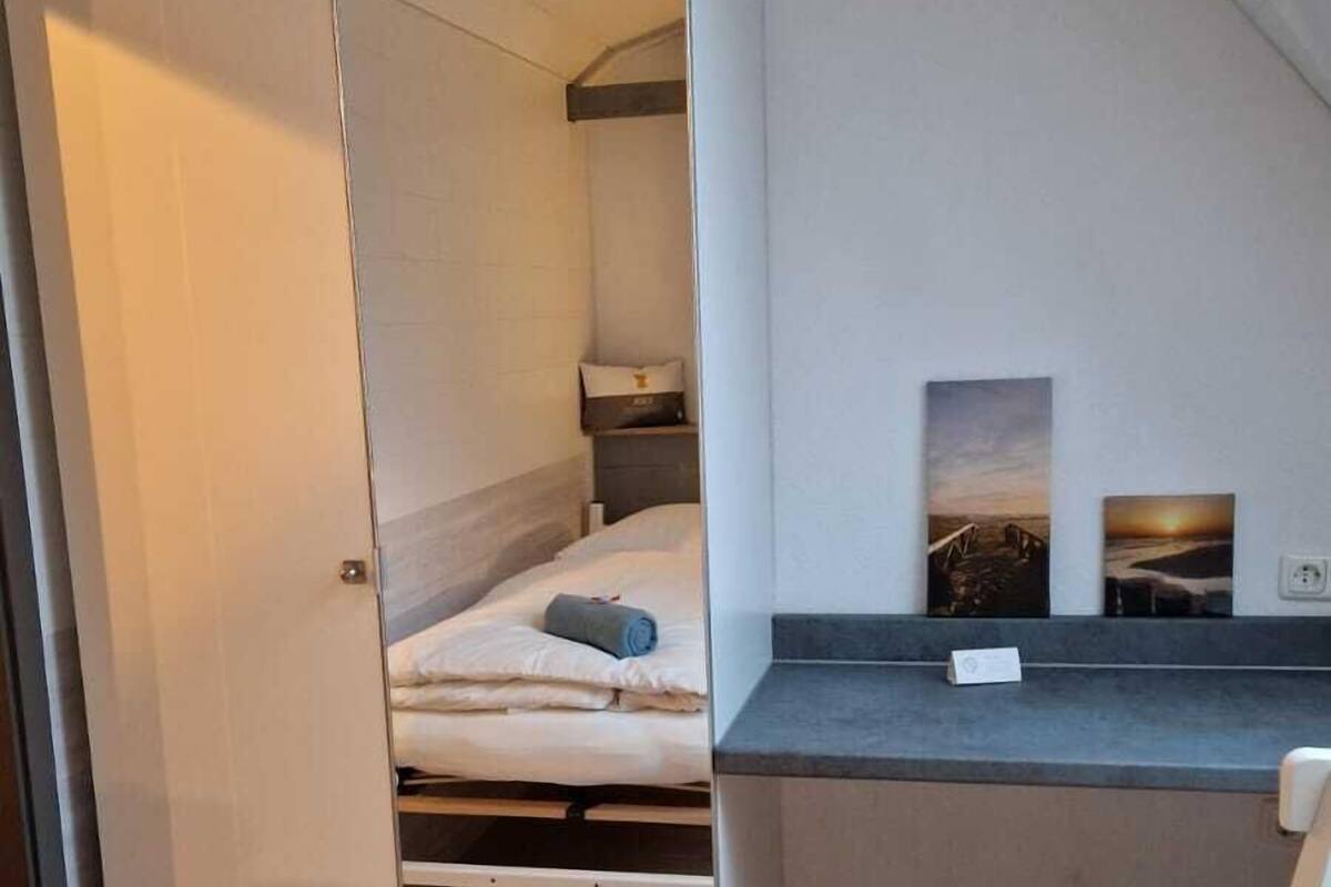 A modern bedroom with a bed, a desk, and a chair. There is a wardrobe and a window with a view of the outside.