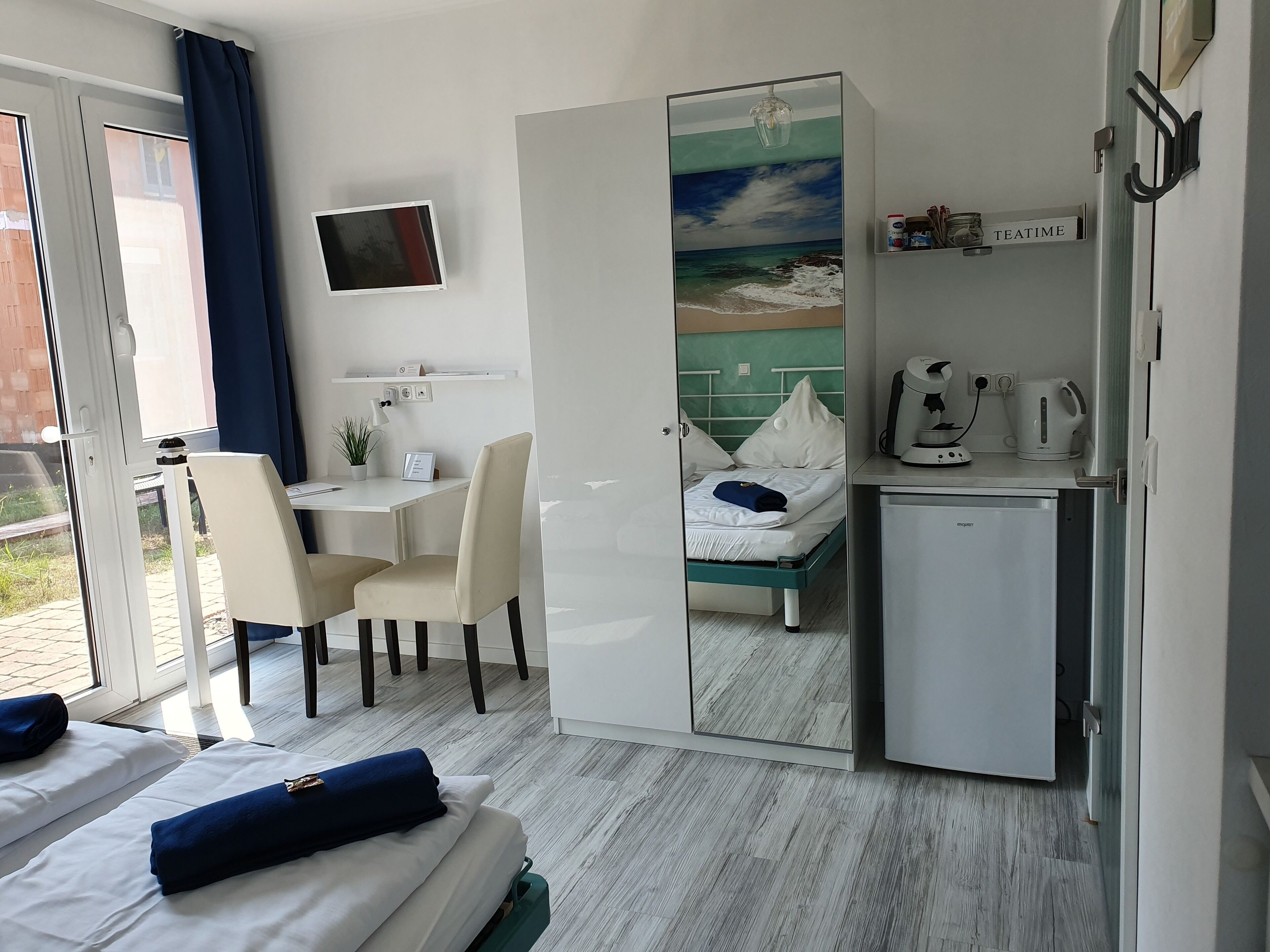 Habitación de hotel con cama, escritorio con silla, kitchenette pequeña y televisor en la pared.