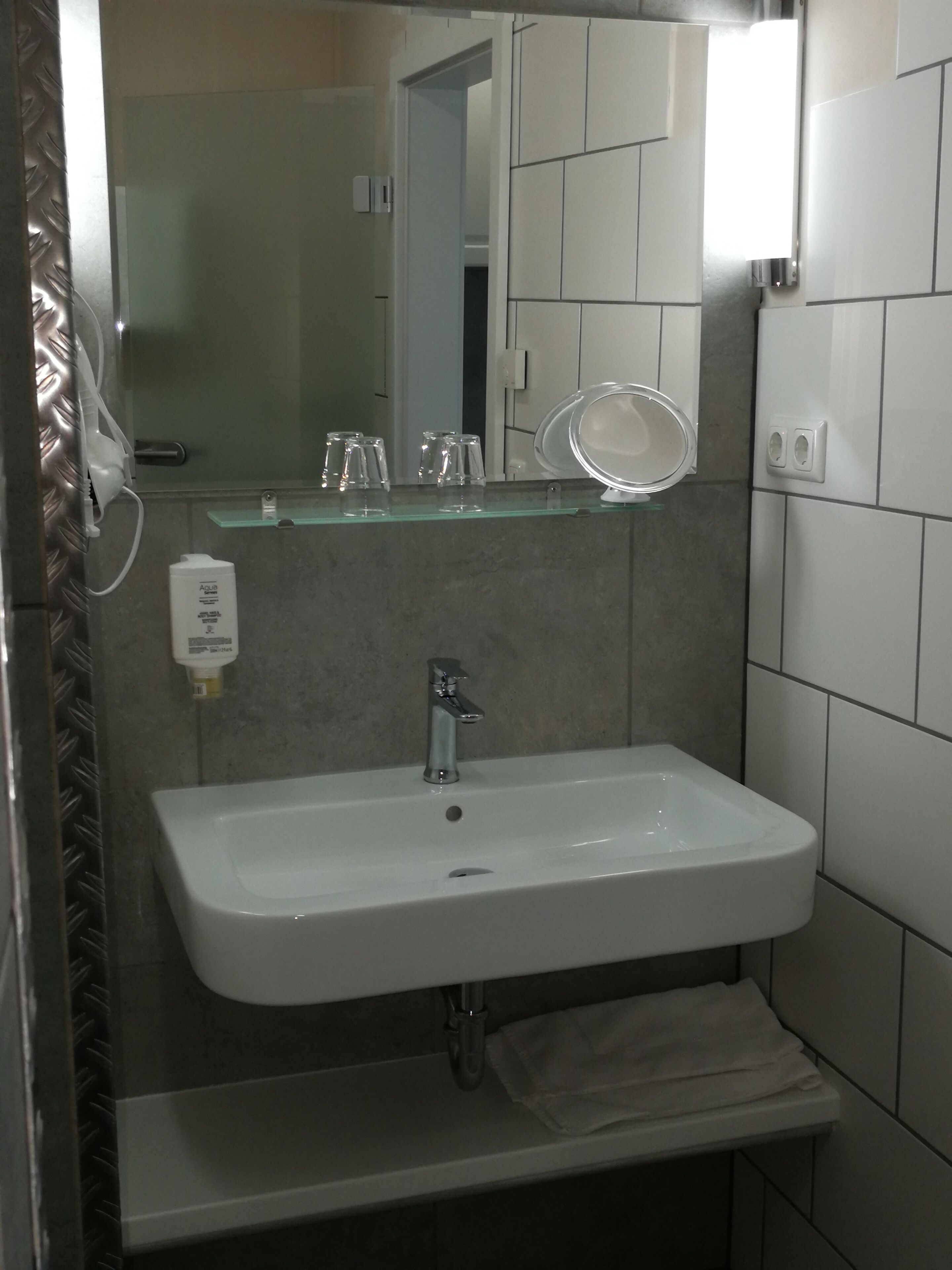 Ein Badezimmer mit Waschbecken, Spiegel und Ablagefläche aus Glas.