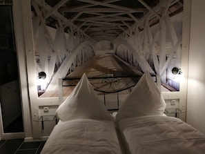 Una stanza con un letto, un tavolino in vetro e vista su un pavimento di legno attraverso una finestra.