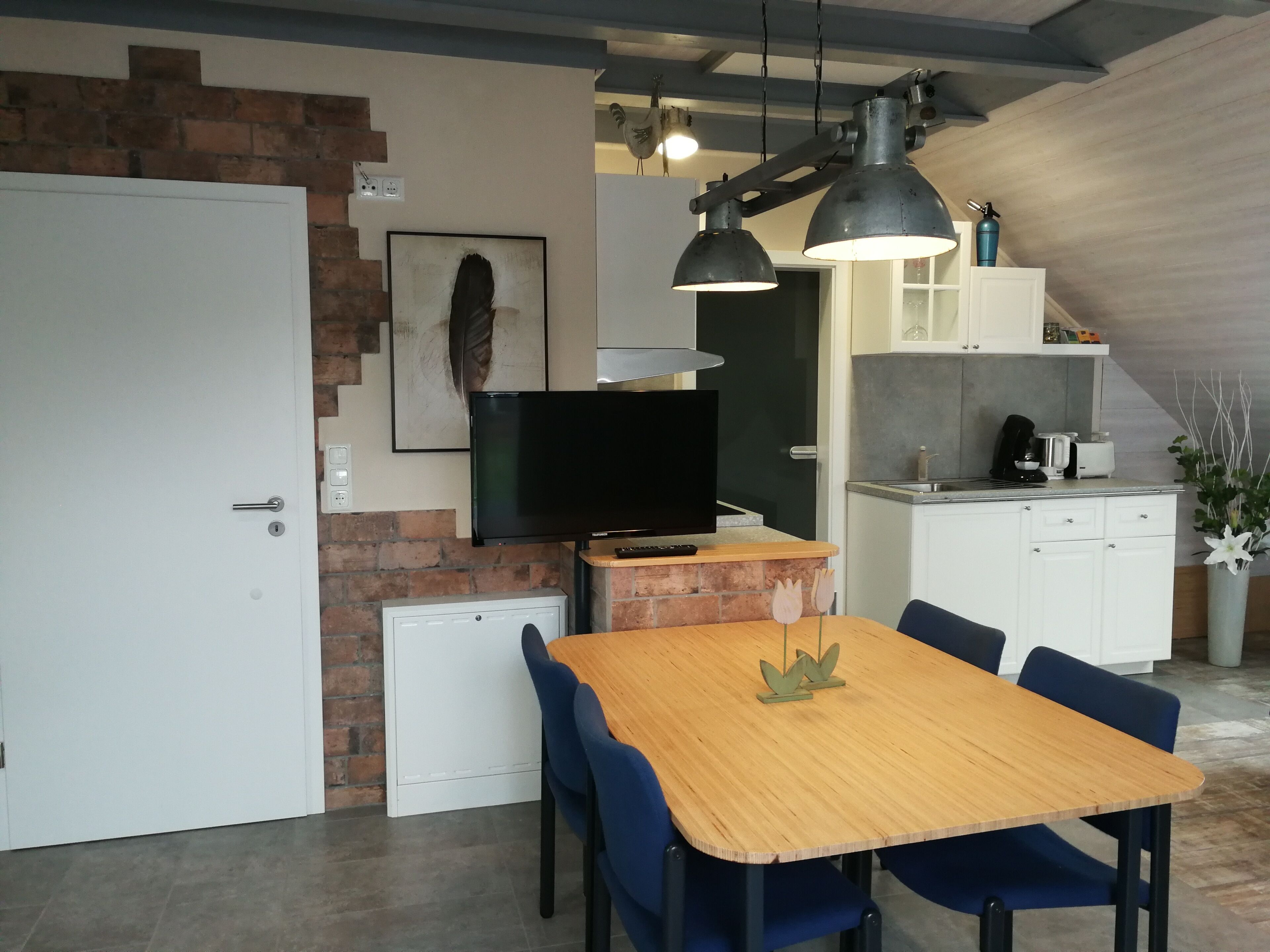 Eine moderne Küche mit einem Holztisch, blauen Stühlen, einem Fernseher und einer Ziegelwand.