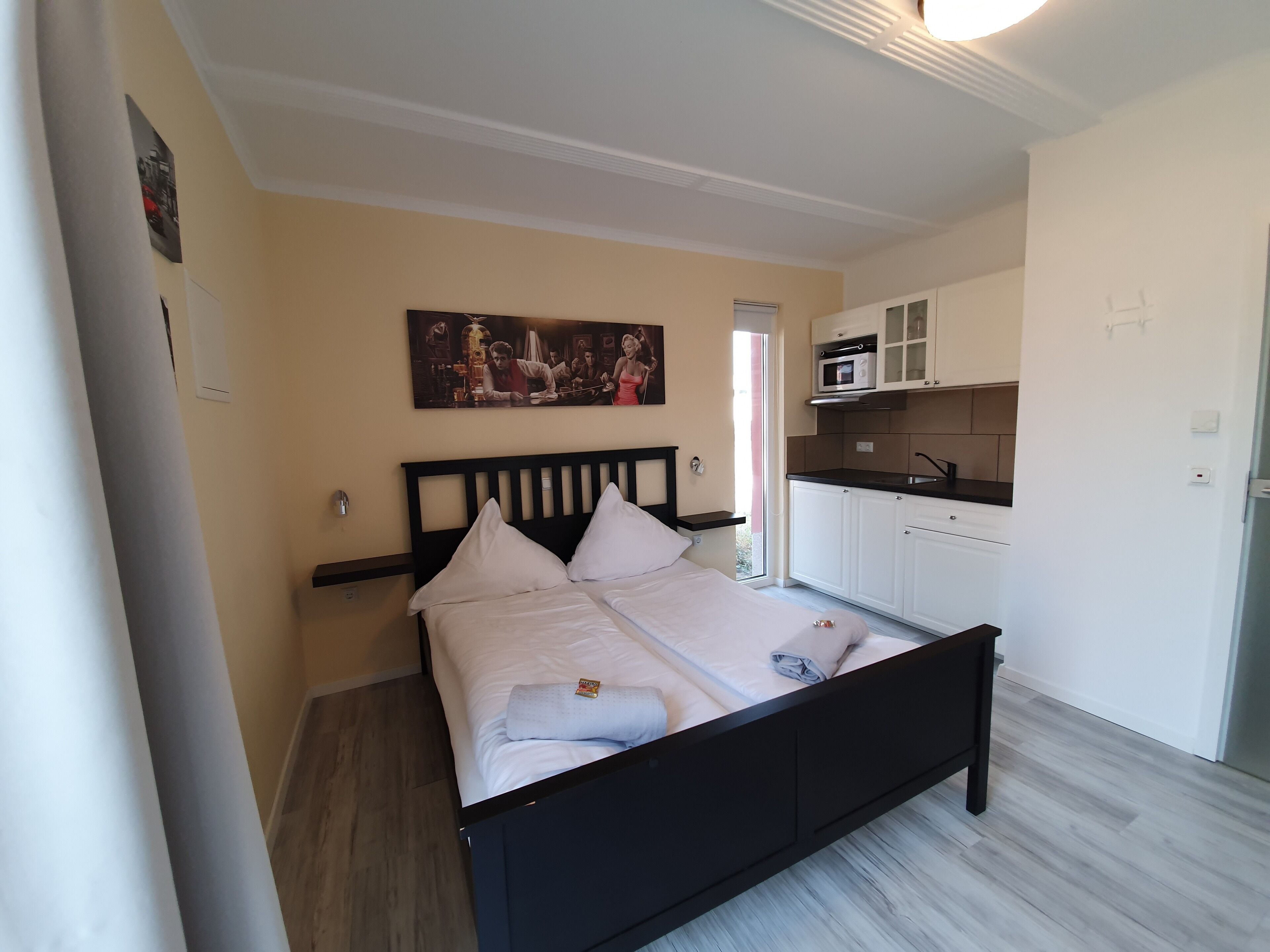 Un dormitorio con cama, un cuadro, una zona de cocina y una puerta.