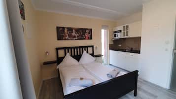 Un dormitorio con cama, un cuadro, una zona de cocina y una puerta.