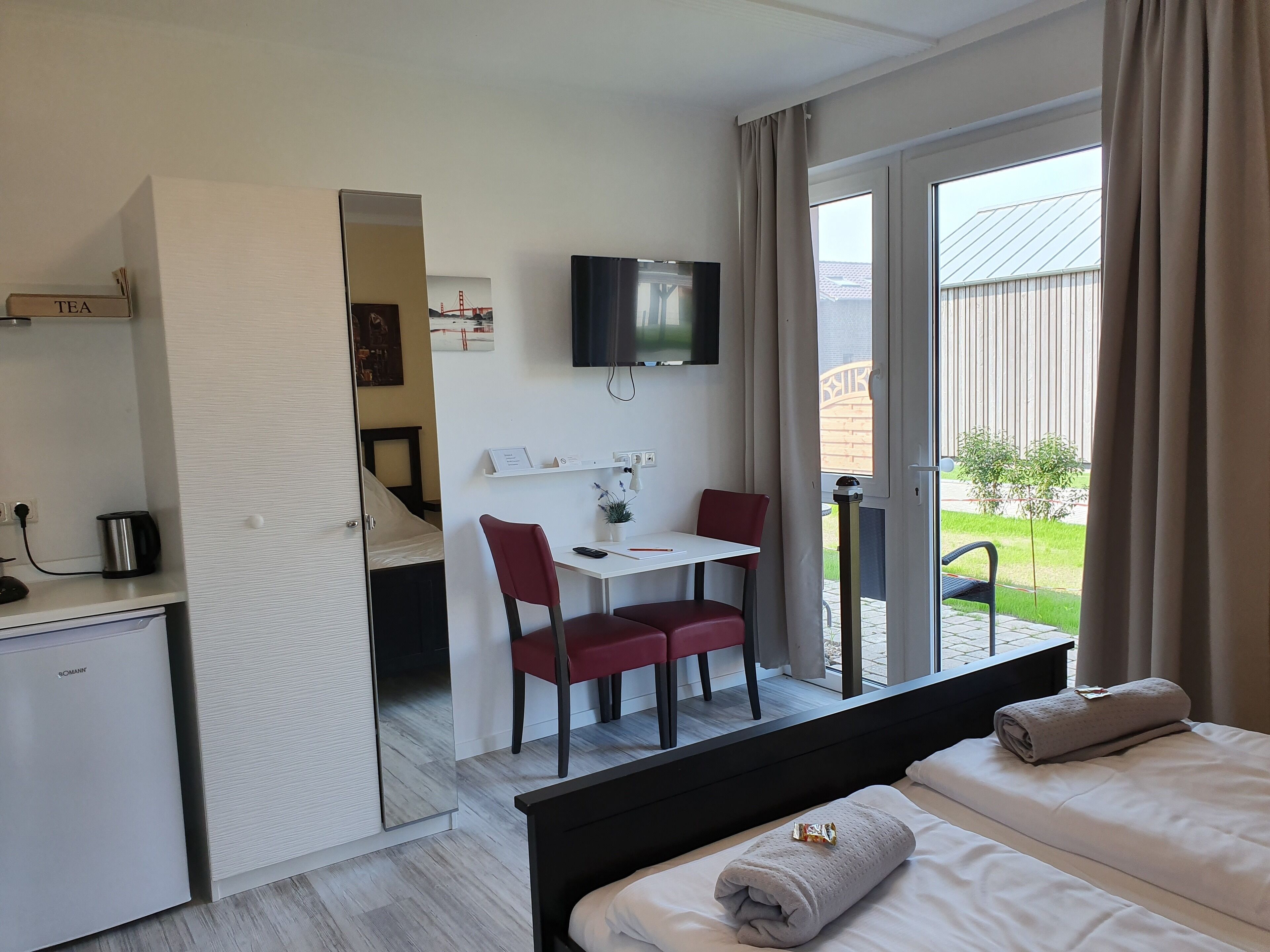 A hotel room with a bed, a desk with a chair, a TV, and a view of the outdoors.