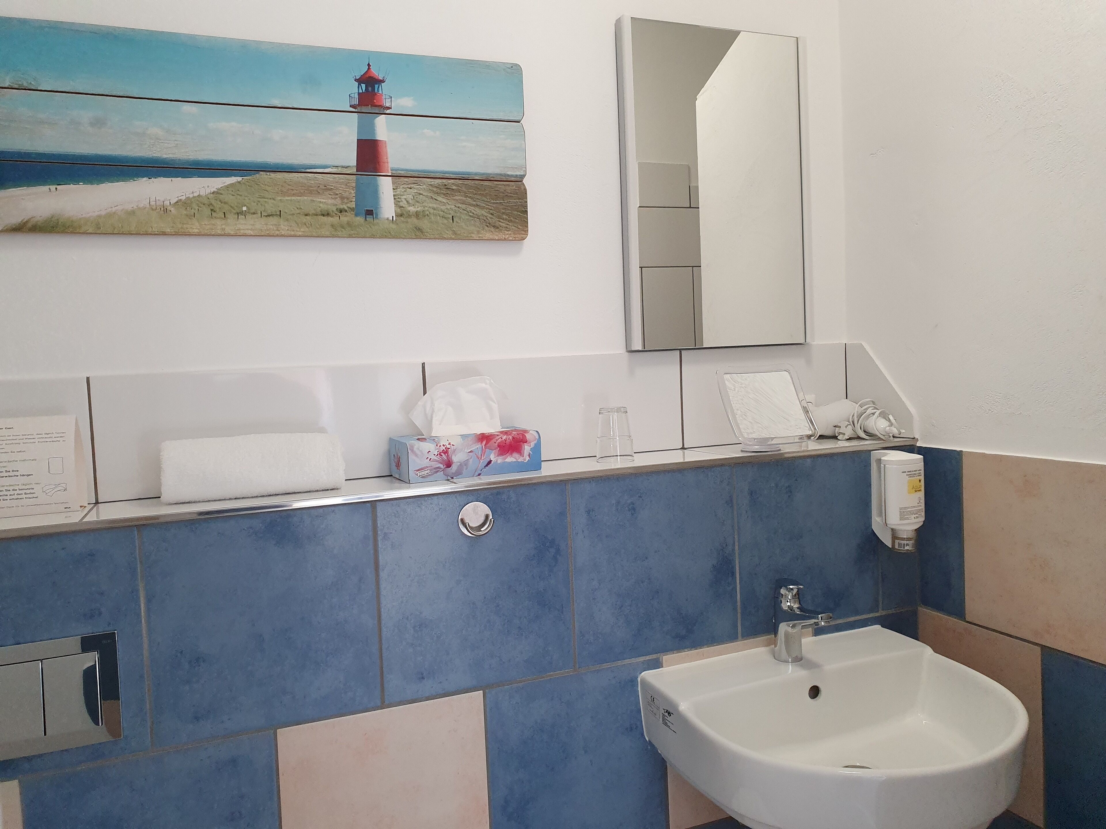 A bathroom with a sink, mirror, and a painting of a lighthouse.