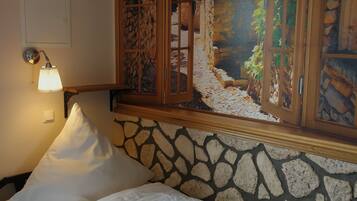 A bed with white linens, a stone wall, a wooden window frame, and a wall-mounted lamp.