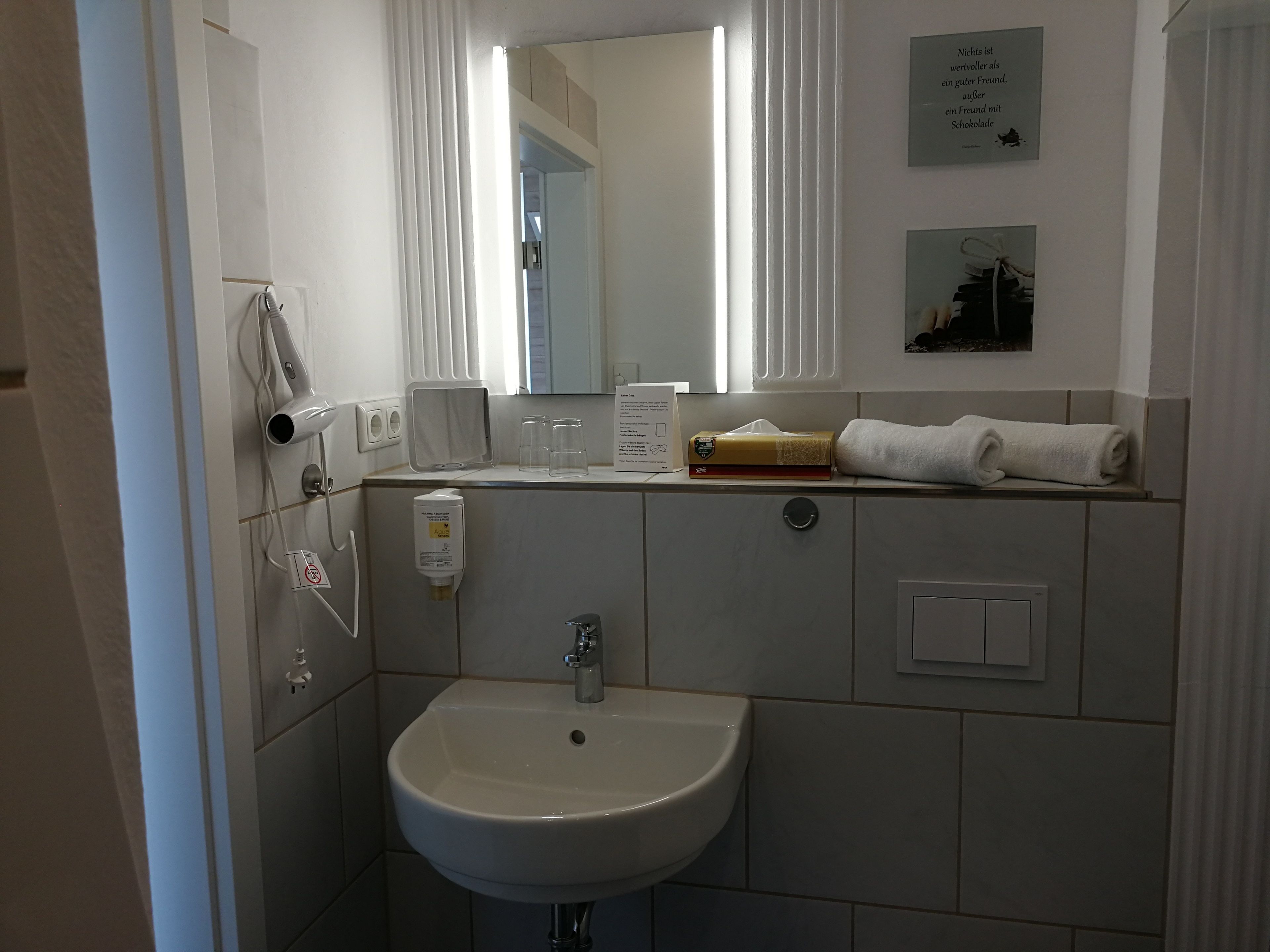 Een badkamer met een wastafel, spiegel, handdoek en een klein plankje met zakdoekjes en glazen.