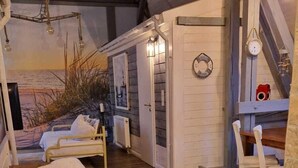 A cozy, rustic interior with wooden floors, a bed with a white blanket, a wooden bench, and a dining area with a table and chairs. - Apartmenthaus in Walle (Schwülper)