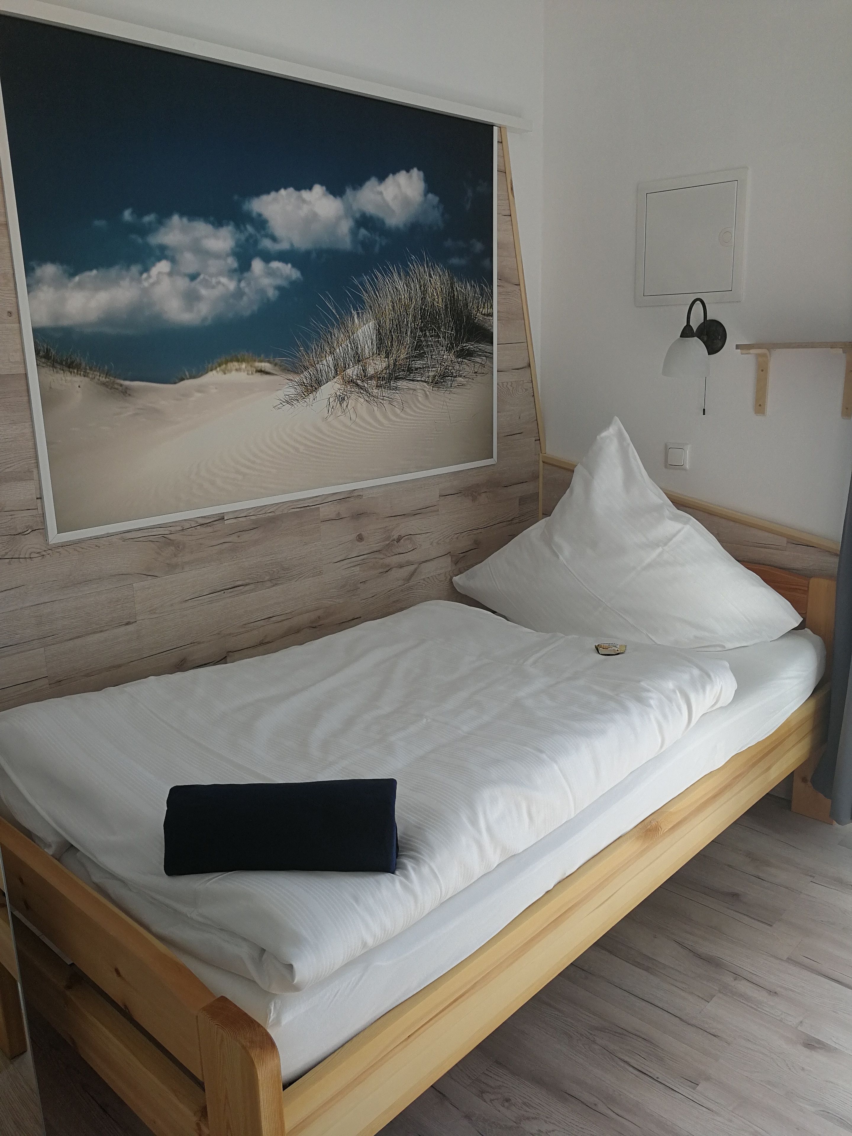 A bed with white bedding, a black pillow, and a large framed picture of a beach scene on the wall.