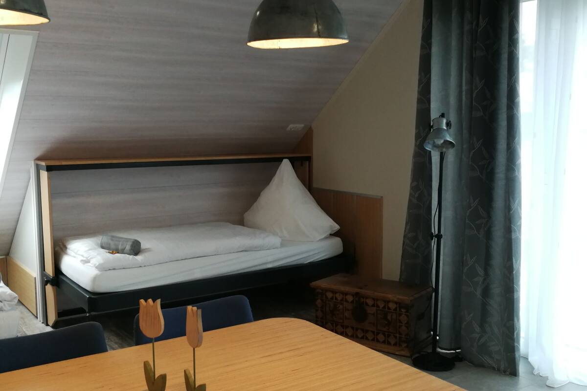 A compact room with a bed, a wooden table, and a floor lamp.