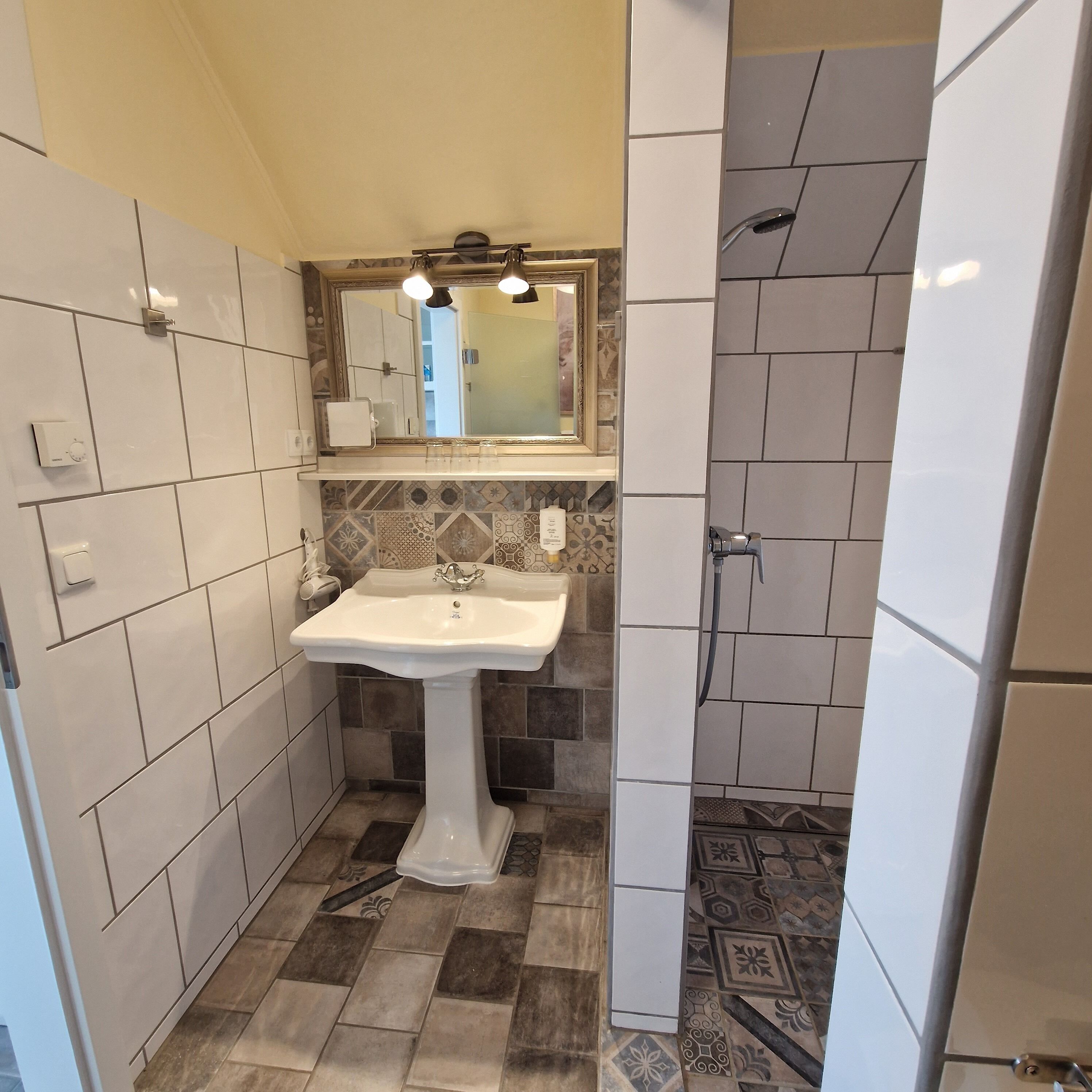 Ein Badezimmer mit einem Standwaschbecken, einem Spiegel, einer Dusche und fliesenbesetztem Boden.