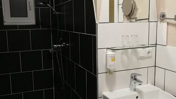 Een badkamer met zwart-witte tegels, een douche met handdouche, een wastafel met spiegel erboven en een klein plankje met toiletartikelen.